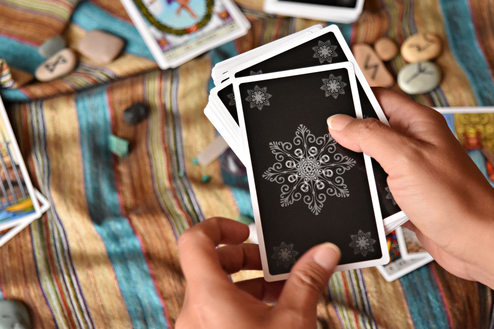 Mains tenant des cartes de tarot lors d'une lecture, entourées de runes et de pierres
