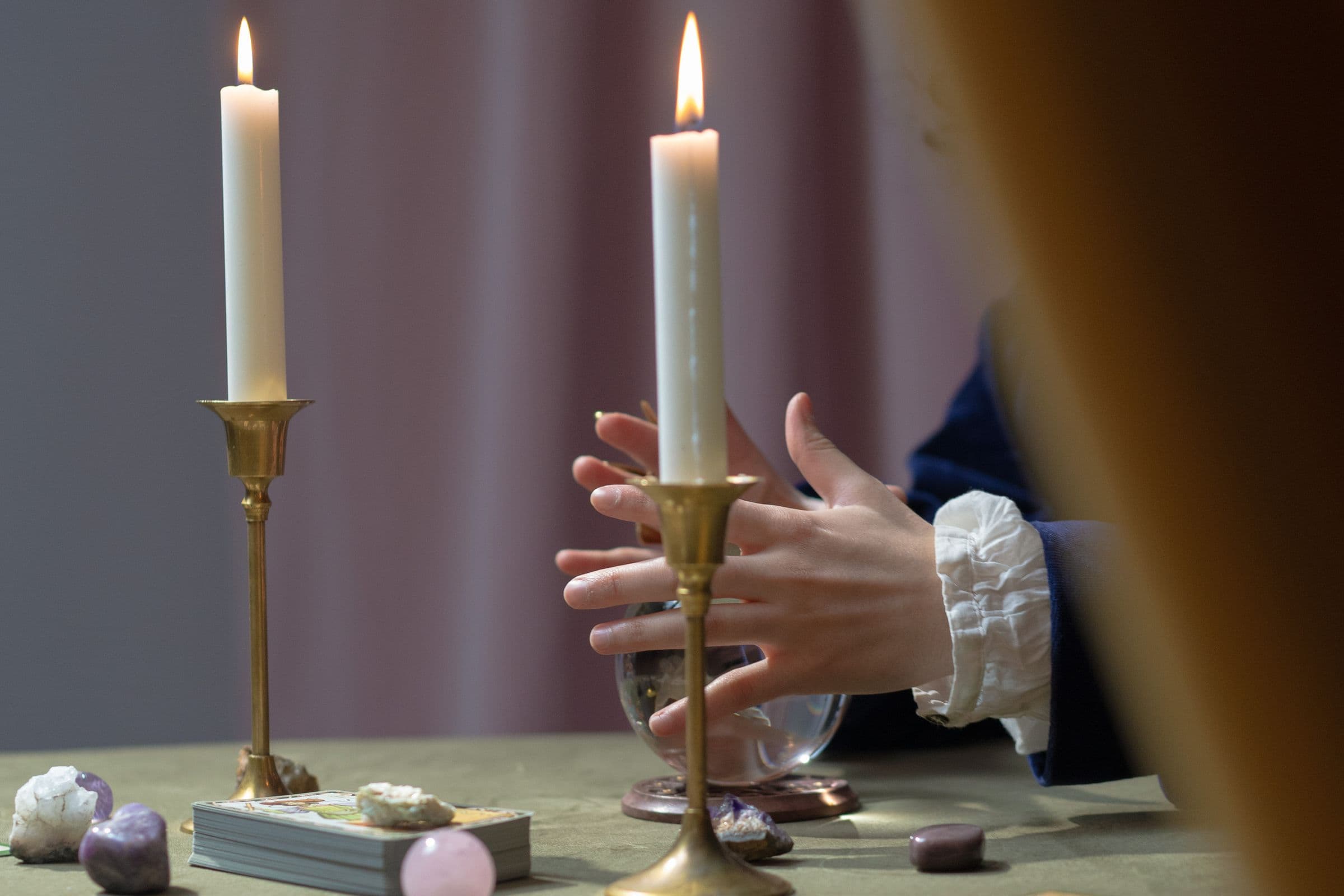 Lecture de voyance : mains posées sur une boule de cristal entourée de bougies et de cartes de tarot